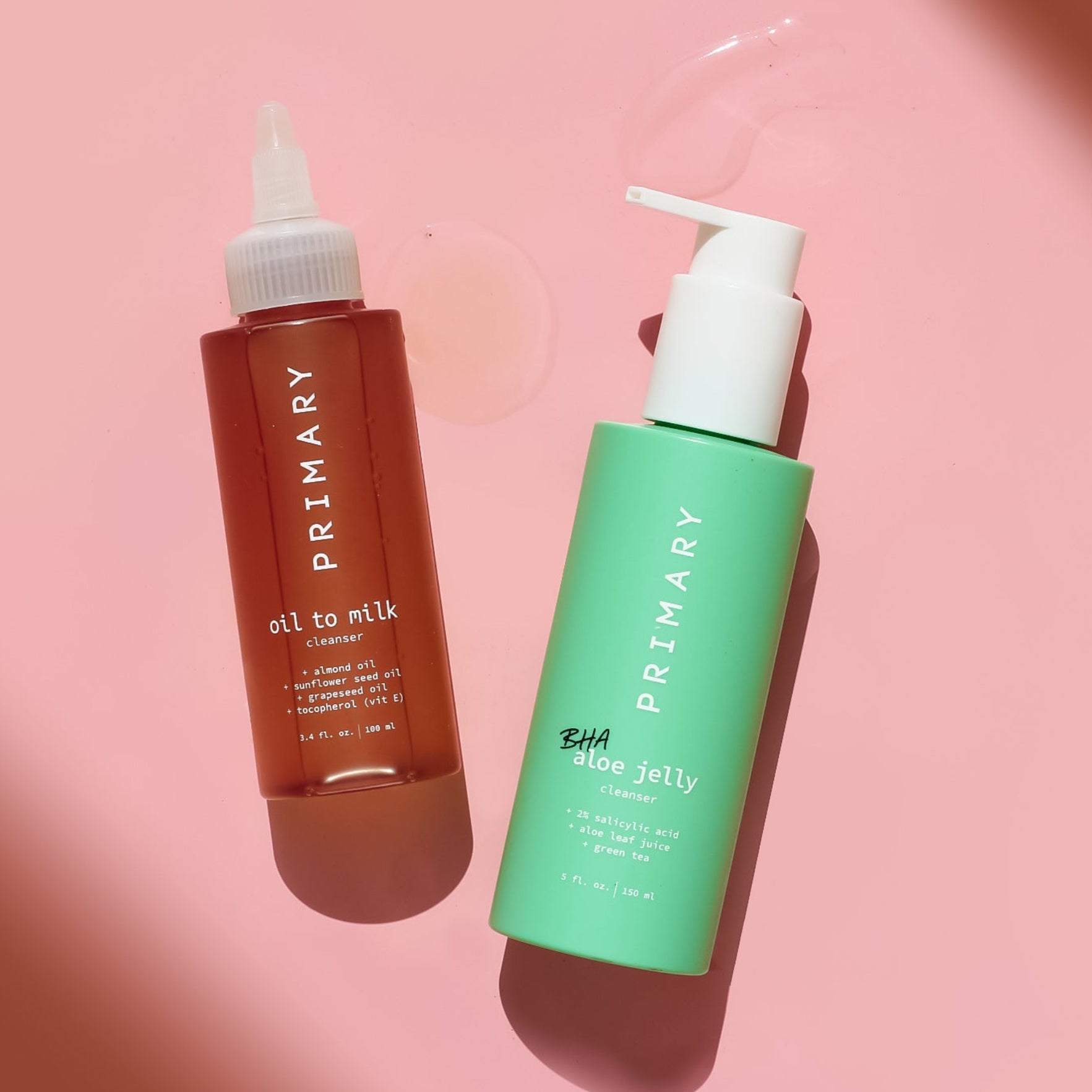 Two bottles of 'PRIMARY' skincare products on a pink background